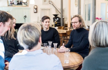Eine Gruppe Menschen sitzt um einen runden Tisch und unterhält sich.