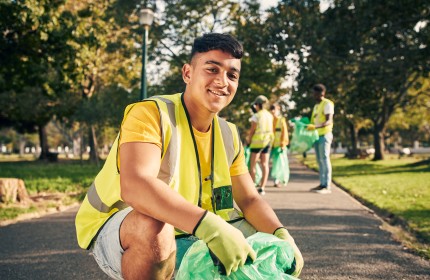 Das Bild zeigt eine Gruppe von jungen Freiwilligen, teilweise mit geringen Deutschkenntnissen, die in einem Park Abfall einsammelt..